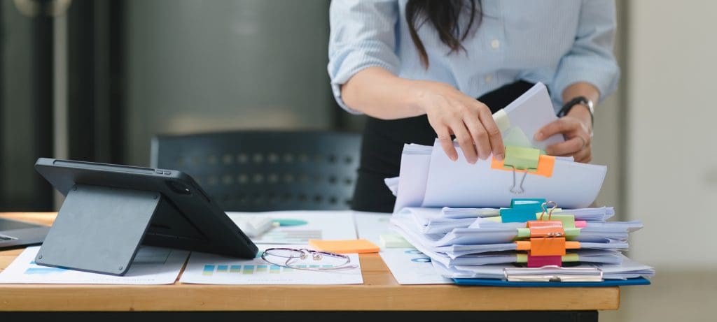 a-businesswoman-is-sifting-through-stacks-of-paper-files-and-folders-that-contain-both-incomplete-and-completed-documents