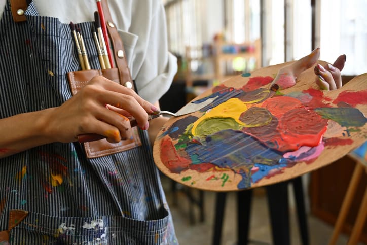 close-up-image-of-a-young-creative-artists-hands-smeared-with-watercolors-holding-a-spatula-mixing-color-on-a-palette